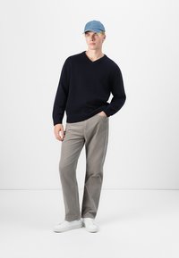 Pull col V marine, pantalon en velours côtelé gris clair, baskets blanches, et casquette de baseball bleu clair. Modèle debout avec une main dans la poche.