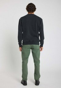 Sweat-shirt noir avec un col rond, des poignets et un ourlet côtelés. Associé avec un pantalon vert et des chaussures noires à lacets. Vue de dos.
