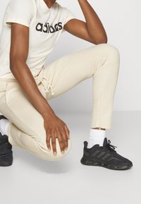 Pantalones deportivos beige con cordón, combinados con una camiseta blanca de manga corta con letras negras y zapatillas deportivas negras.