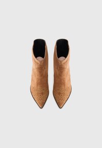 Botas de tobillo de ante color beige con punta afilada, que presentan bordados de tachuelas doradas en la zona de la punta y un interior negro suave.