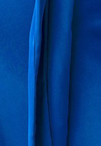 Helderblauwe stof met een gladde textuur en overlappende lagen. Het materiaal heeft een zachte glans en ziet er lichtgewicht uit.