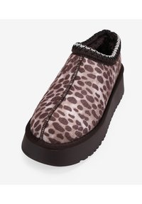 Zapatilla de leopardo con parte superior de piel sintética marrón, una suela de goma marrón gruesa y un borde decorativo en negro y plata a lo largo del cuello.