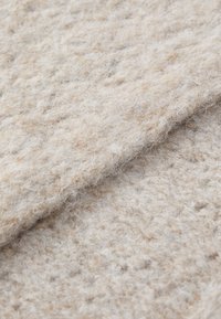 Gros plan sur un tissu tricoté beige plié, avec une texture duveteuse et douce et un motif tissé visible.