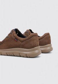 Baskets en cuir marron avec une finition texturée, profil bas, semelle beige rembourrée et accents cousus au niveau du talon et de la zone de laçage.