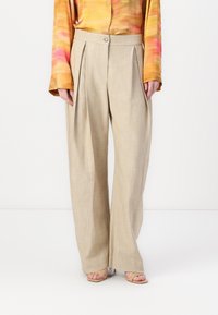 Pantalons larges taille haute beiges avec des plis à l'avant, associés à un blouse à manches longues orange et rose et des sandales à talons beiges.