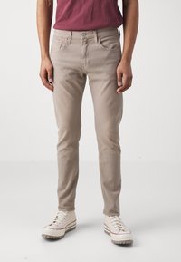 Jeans skinny beige claro de denim, con cinco bolsillos, cremallera y costuras sutiles. Combinados con zapatillas blancas.