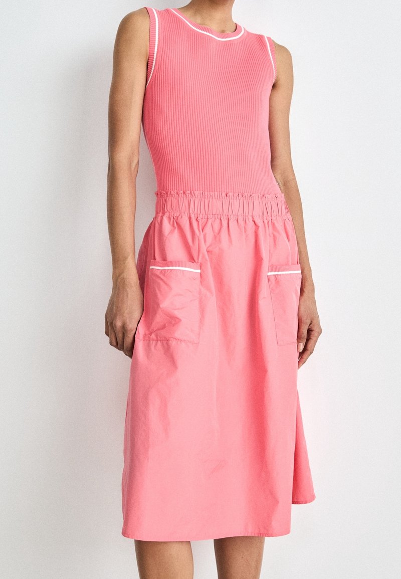 Robe rose côtelée sans manches avec une taille élastique, deux poches avant et des détails en bordure blanche au niveau de l'encolure et des poches.