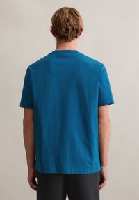 Koszulka z krótkim rękawem w jednolitym kolorze morskim, wykonana z miękkiej bawełny. Posiada okrągły dekolt i luźny krój. Prosty dół z płaskim szwem.