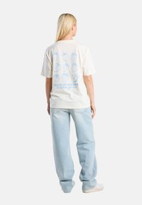 Cream-colored t-shirt with blue strawberry graphic pattern on the back, text "Taste of Summer" and "Garden Grove," paired with light blue jeans.