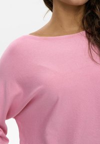 Suéter rosa claro con un escote amplio y un tejido suave y texturizado. El diseño incluye mangas holgadas y una silueta relajada.