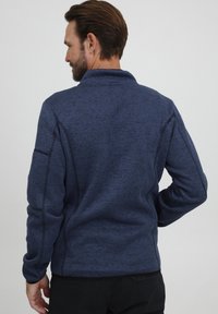 Marineblaue Fleecejacke mit hohem Kragen, strukturiertem Stoff, kontrastierenden Nähten und seitlichen Paneeldetails. Rückansicht, die Passform und Design zeigt.