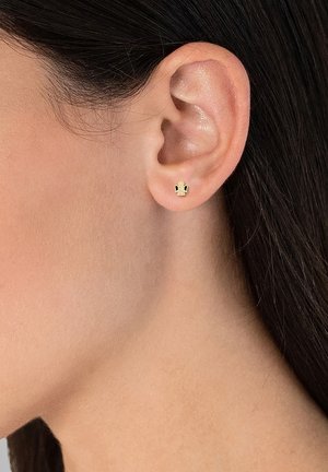 Goldene Steckerohrringe mit einem kleinen Design und schwarzen Akzenten, auf einer strukturierten Oberfläche platziert, die am Ohrläppchen getragen werden.