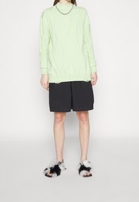 Ljusgrön oversized tröja med vågig texturdesign, matchad med svarta knä-långa shorts och fluffiga svart-vita tofflor.