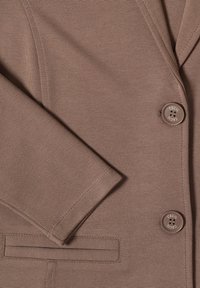 Manche de blazer marron texturé, deux boutons assortis étiquetés "CECIL," et une petite poche passepoilée visible sur le côté avant.