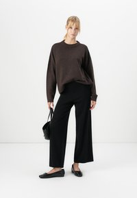 Smeđi oversized pulover, crne široke hlače, crne balerinke i crna torba. Ova kombinacija je ležerna i karakterizira je opušteni kroj i jednobojne boje.