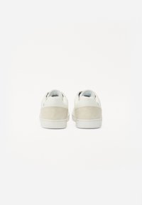 Valged nahast spordijalatsid suede kanna, ümar kujundus ja paksud valged tallad. Kingadel on minimalistlikud detailid ja siledus.