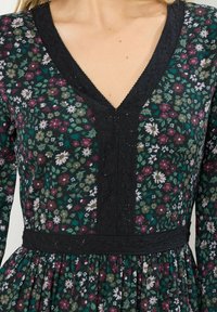 Vestido con estampado floral en verde oscuro y negro, con escote en V, decoración de encaje y una falda con recogido y cintura ajustada.