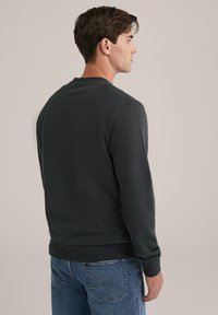 Hanorac gri închis, fabricat dintr-un material moale, cu guler rotund, mâneci lungi și manșete cu nervuri, combinat cu blugi albaștri.