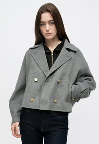 Sivá dvojradová skrátená bunda z vlny so zlatými gombíkmi, širokým klopami a spustenými ramenami. Nosená cez čierny top so zipsom.