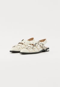 Hvite lær slingback-sko med metallspenner, avrundet tå og svart yttersåle. Har utskjæringsdesign og minimalistiske aksenter.