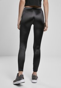 Zwarte legging gemaakt van een glad, rekbaar materiaal met een hoge tailleband. Gecombineerd met grijze sportschoenen met een textuurontwerp.