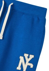 Niektóre niebieskie dresy z żebrowanym paskiem w talii i białymi sznurkami. Na dolnej części lewego nogawka znajduje się duże białe logo NY. Miękka tekstura materiału.