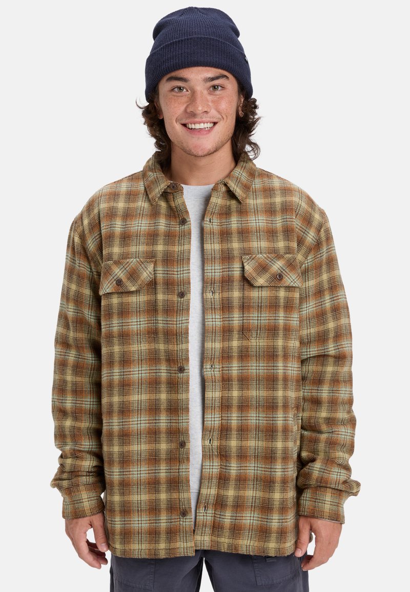 Braun-gelb kariertes Flanellhemd mit zwei Brusttaschen, Knopfleiste und langen Ärmeln, getragen über einem hellgrauen T-Shirt.