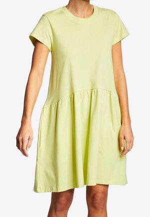 Kobieta ubrana w krótką, żółtą, luźną sukienkę z marszczoną talią i długością do kolan.