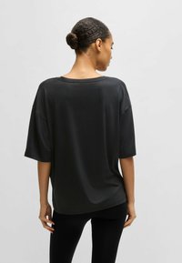 Black oversized T-shirt with short sleeves, smooth texture, and a wide neckline, paired with black leggings. Simplistic, loose fit design.