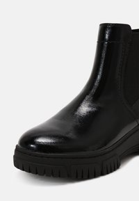 Black leather ankle boot with a glossy finish, elastic side panels, and a textured black rubber sole featuring zigzag patterns.