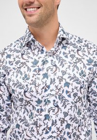 Camicia bianca a maniche lunghe con un dettagliato motivo floreale e di uccelli in tonalità blu e marrone, con colletto standard e chiusura a bottoni.