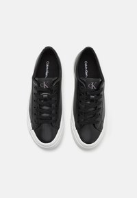 Svarte skinn sneakers med hvite gummisåler, med svarte snører og en logotag på tungen. Barberte overflater, avrundet tådesign.