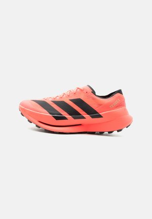 Lys koral trail løbesko med sorte Adidas-striber, klodset sål og "TERREX" branding på hælen.