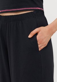 Černé, lehké kalhoty s elastickým páskem, které mají boční kapsu a kontrastní růžové prošití na lemu. Měkká textura.