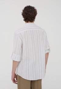 Camicia in lino bianco con leggere righe verticali, maniche arrotolate e orlo arrotondato, dotata di un colletto semplice e una vestibilità comoda.
