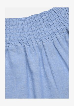 Lyseblåt stofskørt eller bukselinning med elastisk rynkning og opsamlet materiale nedenunder.