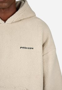 Κρέμα φλις φούτερ με υφή στην επιφάνεια. Διαθέτει το μαύρο λογότυπο "PEGADOR" στο μπροστινό μέρος. Σχεδίαση με κουκούλα για επιπλέον ζεστασιά.