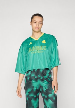 Roheline Adidas Sportswear lühike topp V-kaelusega, lühikeste varrukatega, millel on kollane bränding. Ühendatud mustade ja roheliste mustritega pükstega.