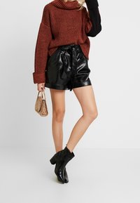 Hedvábný pletený rolák v rezavé a černé pruhy, kombinovaný s vysokými černými šortkami z ekologické kůže s vázáním v pase. Černé kotníkové boty.