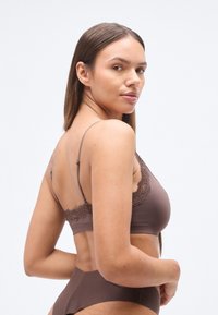 Καφέ bralette με δαντέλα, ρυθμιζόμενους ιμάντες, λείο ύφασμα και άκοπη σχεδίαση, συνδυασμένο με αντίστοιχο σλιπ μεσαίου ύψους.