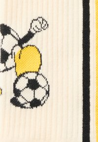 Καρτούν μέλισσα με σφιγμένη γροθιά και ασπρόμαυρη μπάλα ποδοσφαίρου πάνω σε λευκό πλεκτό ύφασμα με μαύρες και κίτρινες ρίγες.