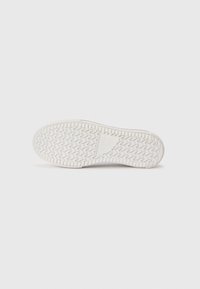 White sneaker sole with zigzag tread pattern and textured surface. Features a flat shape and rounded toe, with minimal design details.