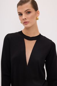 Schwarzes Strickoberteil mit tiefem V-Ausschnitt und langen Ärmeln. Besitzt einen strukturierten Stoff und einen runden Kragen. Das Modell trägt goldene Creolen.