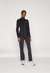 Mustast fliisist tõmblukuga jakk kõrge kraega, kombineeritud mustade pükstega. Modell kannab halli tossusid siniste detailidega. Lihtne, istuv disain.