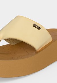 Sandale plateforme beige avec large bride présentant un petit logo métallique « Roxy » et un motif floral embossé sur la semelle.