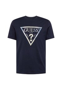 Camiseta de algodón azul marino con un gráfico triangular que presenta el logo "GUESS", detalles en plata en relieve y un diseño de signo de interrogación en el centro.