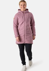 Roze fleece jas met een capuchon, ritssluiting aan de voorkant en zakken. Heeft een gestructureerd oppervlak en lichtbruine toggles. Draagt over zwarte broek.