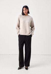 Maglione a maglia di un beige chiaro con maniche lunghe, scollatura rotonda e orlo a coste abbinato a pantaloni neri a gamba larga e scarpe nere a punta.