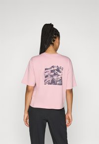 Rosa Baumwoll-T-Shirt mit einem schicken Schnitt, das auf dem Rücken eine dunkelblaue Berggrafik und kurze Ärmel hat.