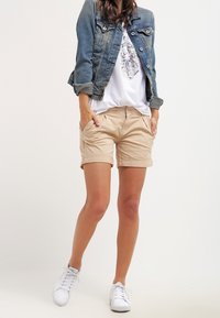 Denim takki, jossa on vaalea pesu, vaaleat rullatut shortsit ja valkoiset lenkkarit. T-paita, jossa on graafinen printti. Rentouttava, väljää istuvuutta oleva muotoilu.